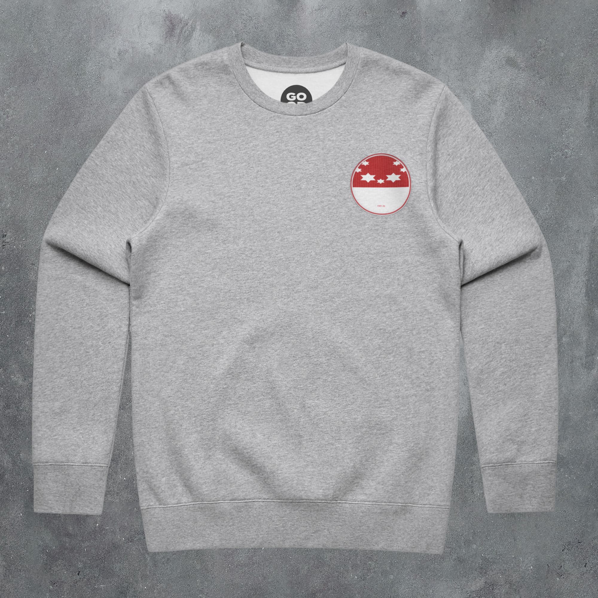 a grey sweatshirt with a red and white patch on the chest